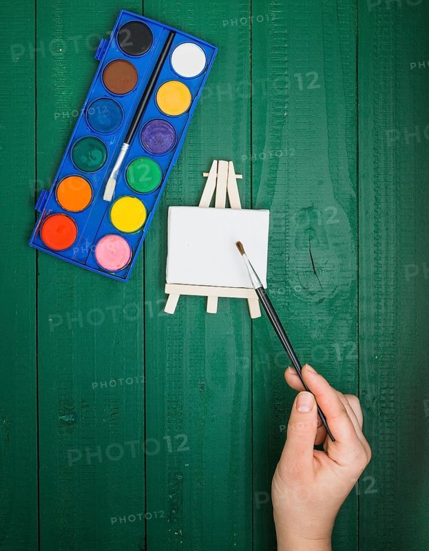 Elevated view hand holding paint brush mini easel watercolor palette