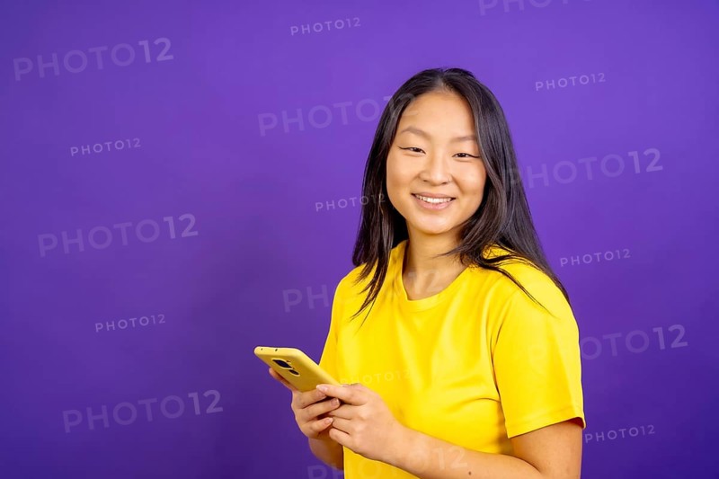 Studio photo with purple background of a chinese woman using phone and smiling at camera