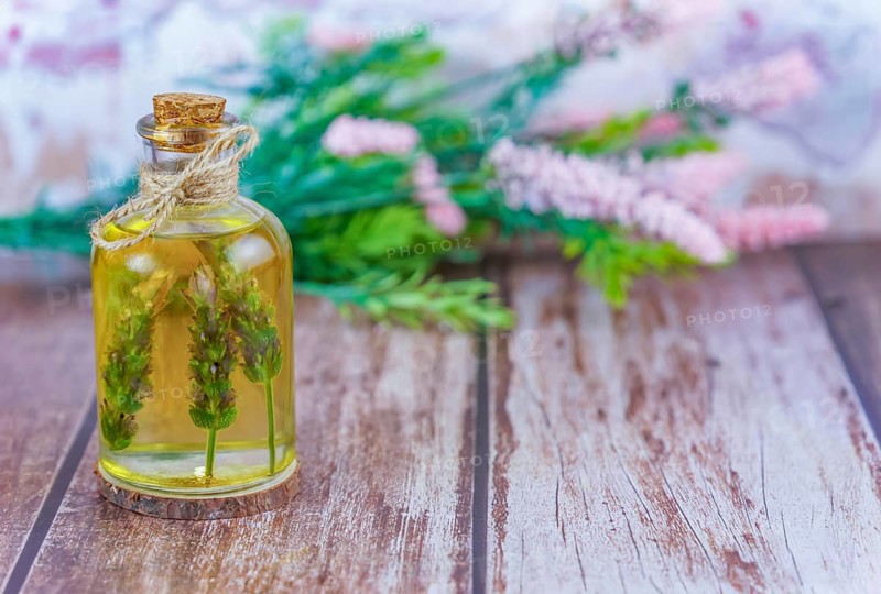 Glass bottle with lavender oil with lavender branches inside on a wooden table