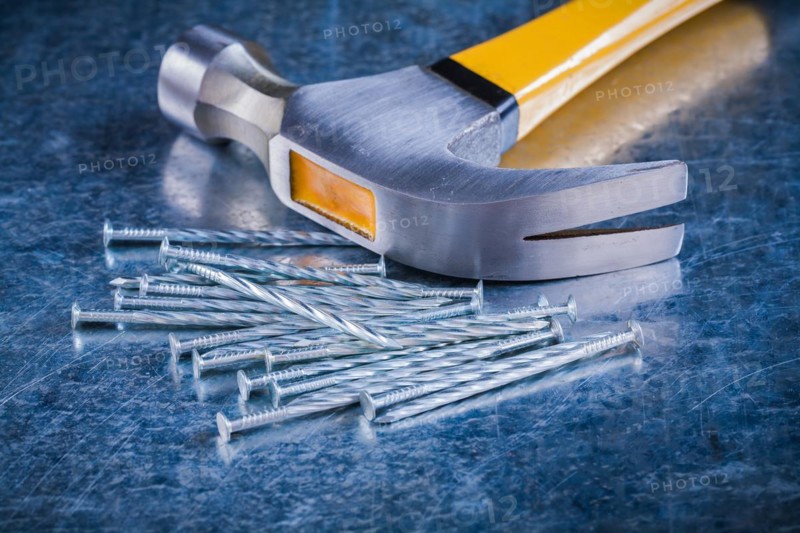Long stainless steel nails with claw hammer on scratched metallic background Maintenance concept
