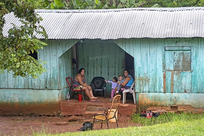 Family posing at wooden hut with corrugated sheet roof in rural village near Ciudad del Este