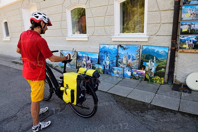 Cyclist looking at kitsch postcards and paintings in front of Hohenschwangau Castle
