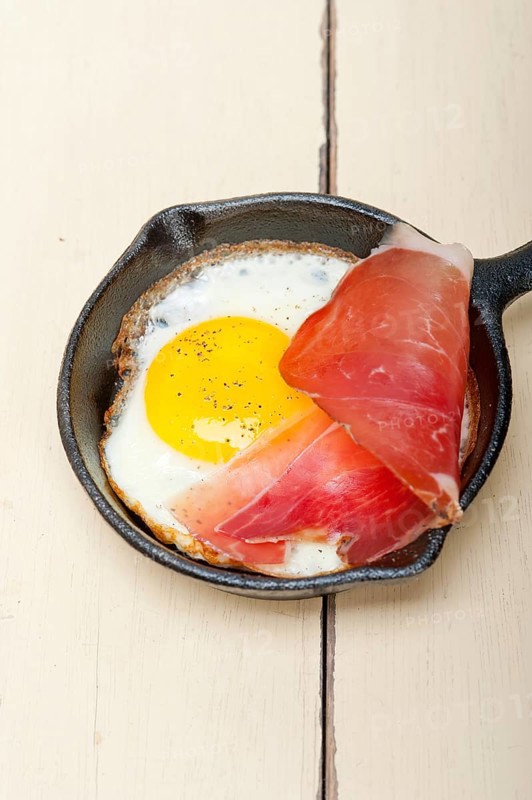 Fried egg sunny side up with Italian tyrolean speck smoked ham on a skillet