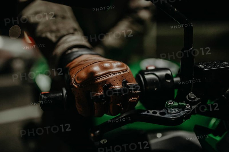 A motorcyclist in brown leather gloves sits on a motorcycle