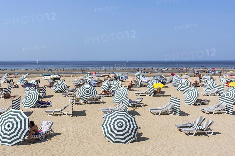 Sunbathers in relax chairs under parasols on the beach at seaside resort along the Belgian North Sea coast during heat wave in summer in Belgium