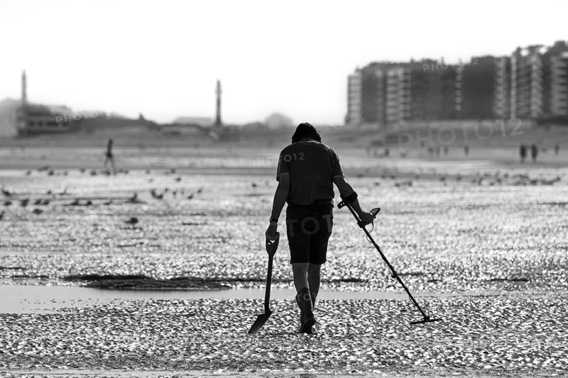 Man with metal detector beachcombing on sandy beach along the North Sea coast on an early morning in summer during the holiday season