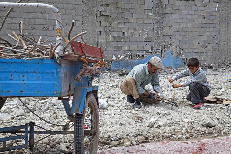 Son helping father recuperating iron with metal saw from debris of collapsed building after earthquake in Van