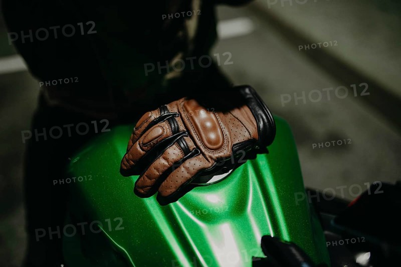 A brown leather motorcyclist glove lies on the tank of a green motorcycle