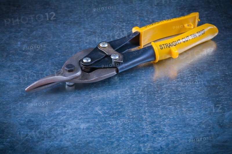 Sheet steel scissors on scratched vintage metallic background close-up construction concept