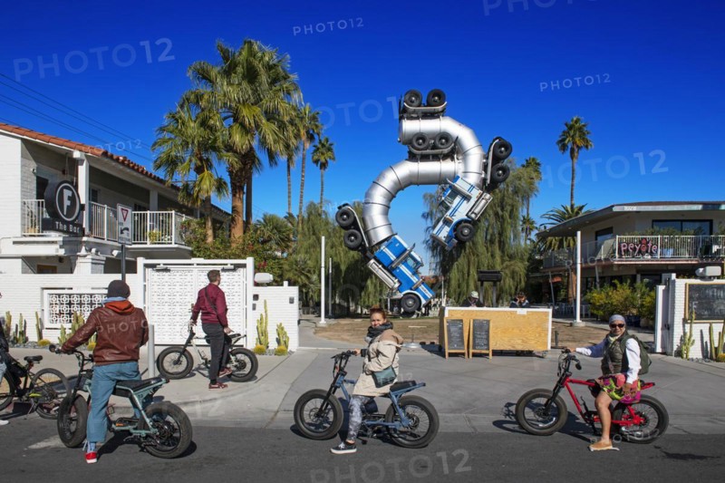 Group of cyclists on a guided tour in front of an artwork made of two art trailers