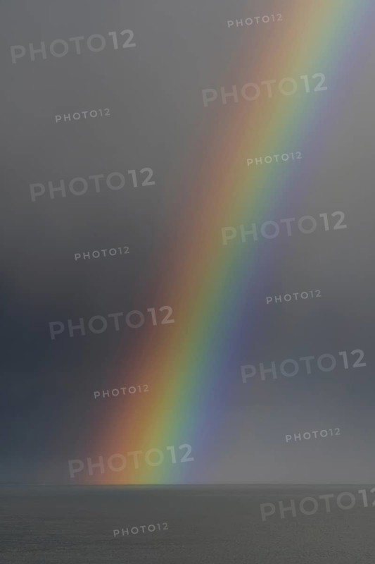 Colourful rainbow over sea water and approaching snow shower along the North Sea coast in winter