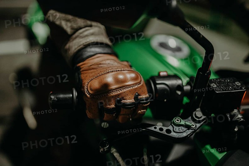 A motorcyclist in brown leather gloves sits on a motorcycle