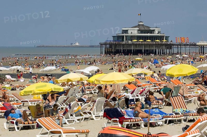 Tourists sunbathing on the beach during the summer holidays and the pier at seaside resort Blankenberge