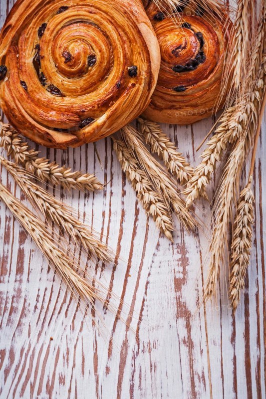 Freshly baked sultana rolls Wheat ears on a vintage wooden board Food and drink concept