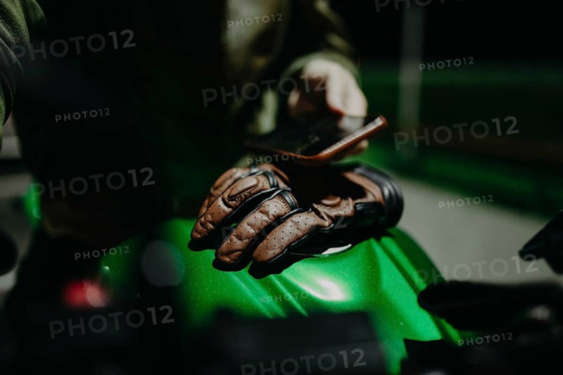 A brown leather motorcyclist glove lies on the tank of a green motorcycle
