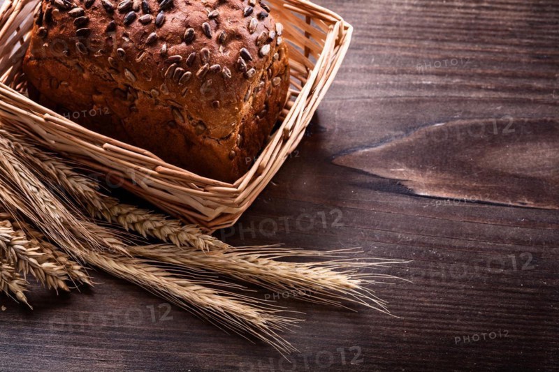 Crusty bread with seeds in wicker basket Wheat ears on vintage pine wooden board Food and drink concept