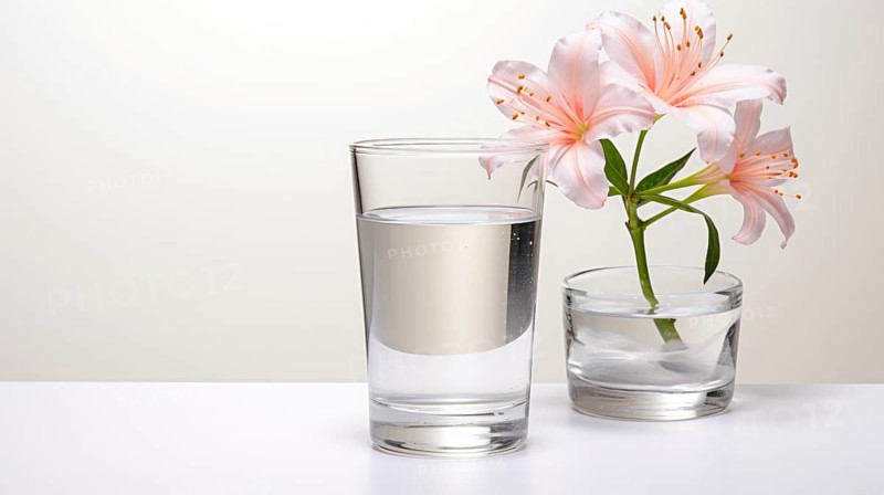 A clear glass of water and a small vase with pink flowers on a white surface illuminated by natural light Ai generated