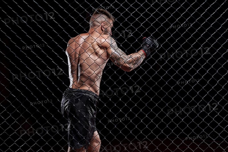 Dramatic image of a mixed martial arts fighter standing in an octagon cage. The concept of sports