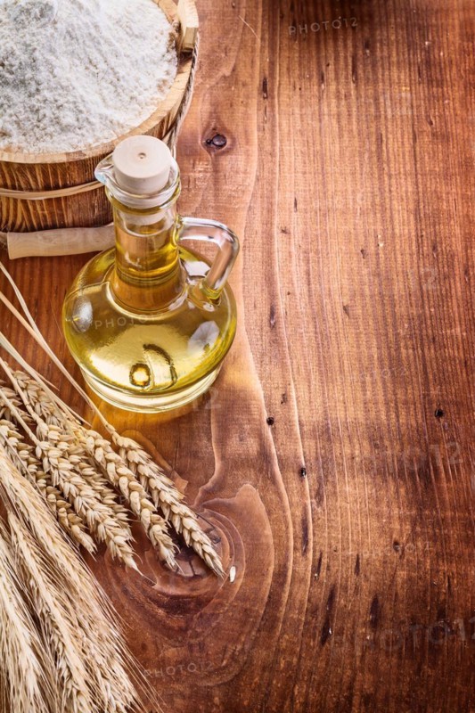 Bottle with oil bucket of flour wheat ears on vintage wooden board with copyspace food and drink concept