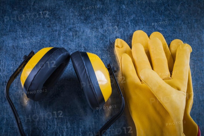 Protective yellow earmuffs and leather gloves on scratched metallic surface construction concept