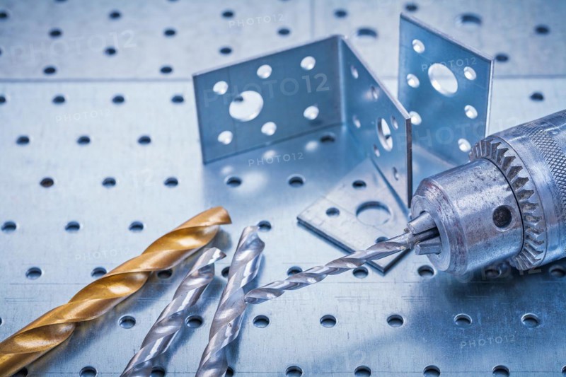 Drill with metal drills and drilled angle bars on a perforated metal background Design concept