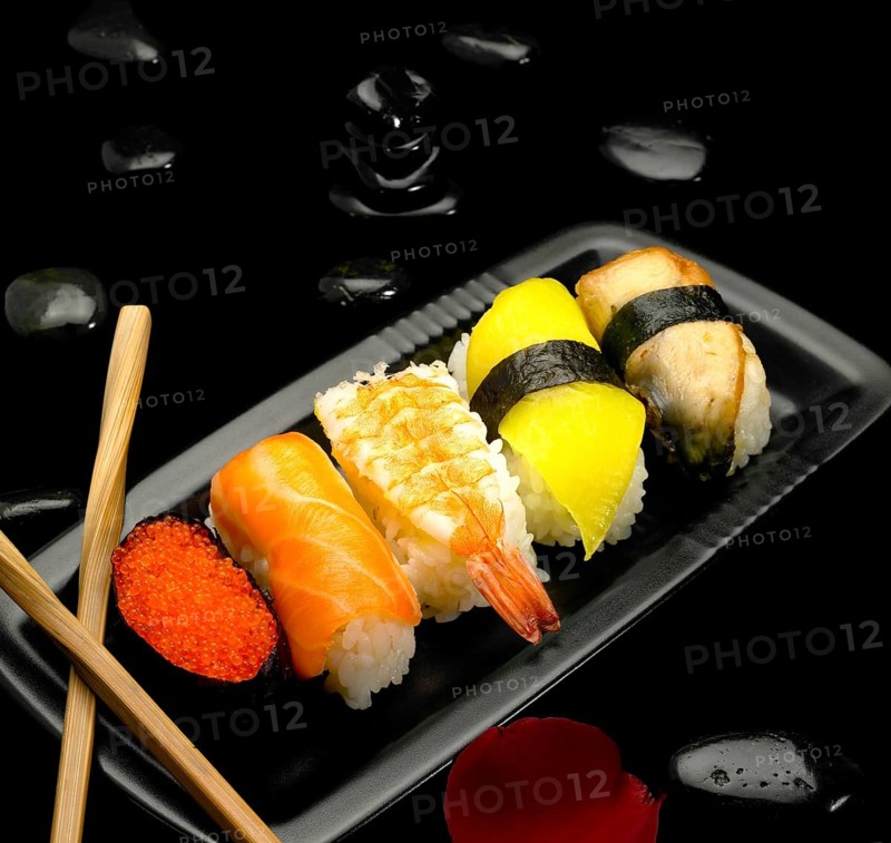 Assorted sushi plate on black pebbles over black background