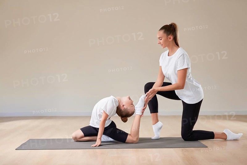 Beautiful female teacher helps a little girl stretch in a gymnastics class. The concept of education