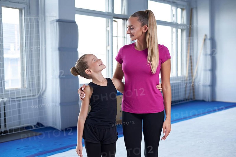 Training in the gym class. A little girl under the guidance of a trainer performs exercises. Gymnastics concept. Mixed media