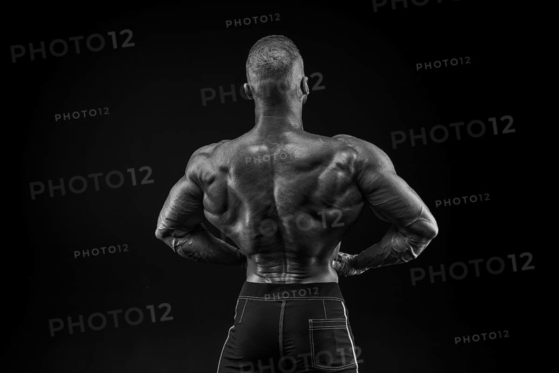 Silhouette of a strong bodybuilder. View from the back. Confident young fitness athlete with a powerful body and perfect abs. Black and white photography. Dramatic light