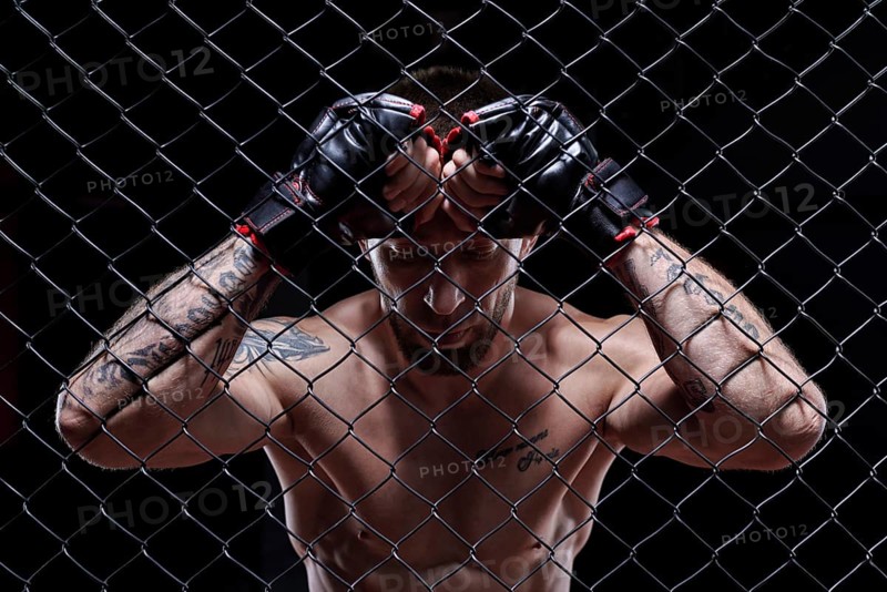 Dramatic image of a mixed martial arts fighter standing in an octagon cage. The concept of sports