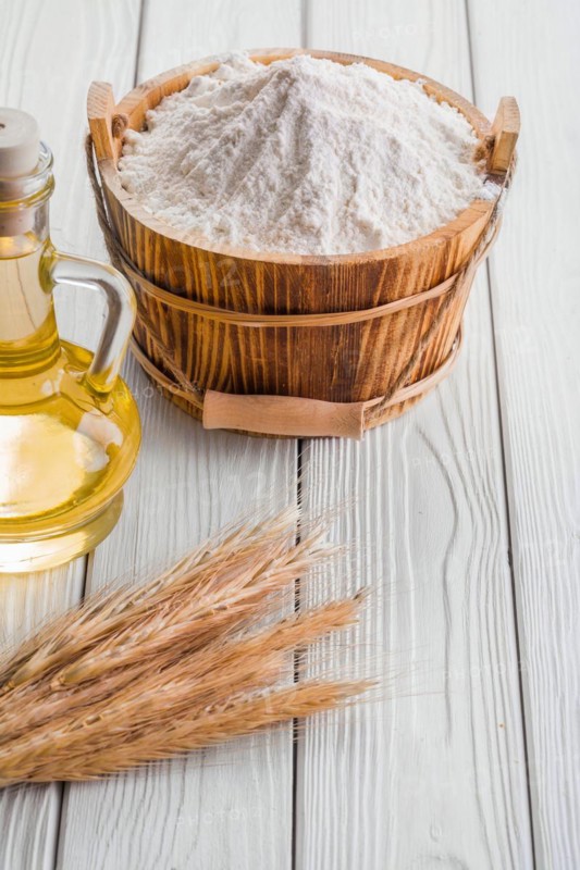 Bucket of flour ears of wheat bottle of oil on old white boards