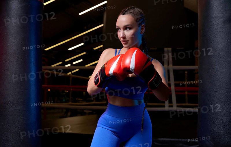 Image of a powerful sportswoman wrestler. Posing in a blue tracksuit and red boxing gloves. The concept of wrestling and boxing. Mixed media