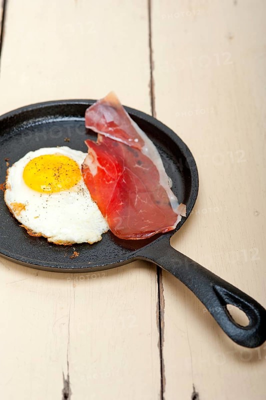 Fried egg sunny side up with Italian tyrolean speck smoked ham on a skillet