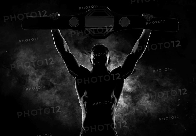 Kickboxer victoriously raises the belt won in the tournament against the backdrop of smoke. Sports competitions. Fight night. The concept of mixed martial arts. MMA