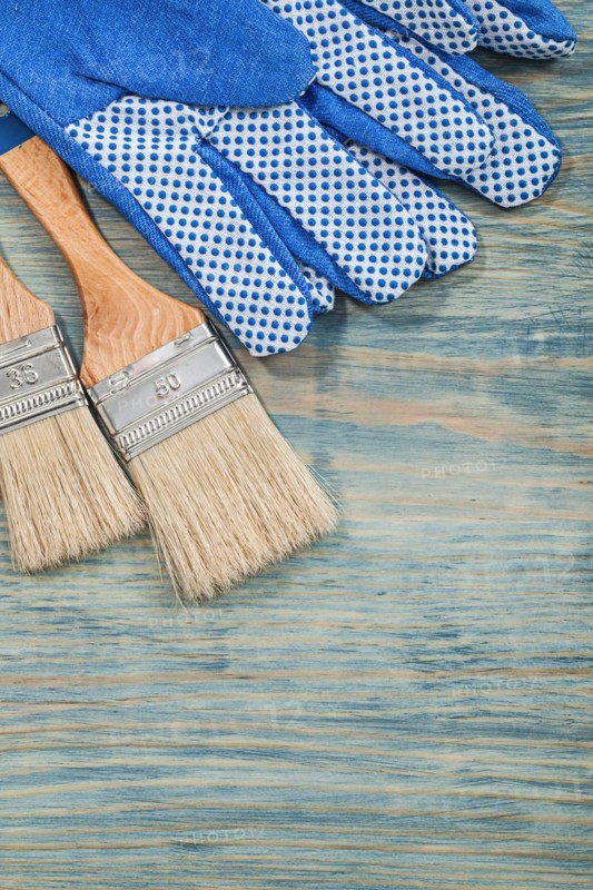 Composition of paintbrushes safety gloves on wooden board construction concept