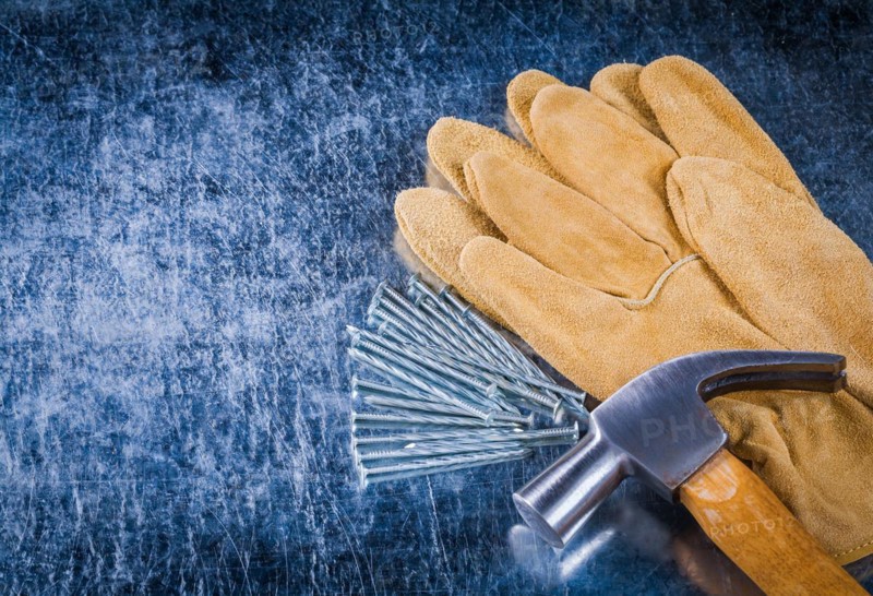 Pair of leather protective gloves construction nails and claw hammer on scratched metallic background copy space image building concept