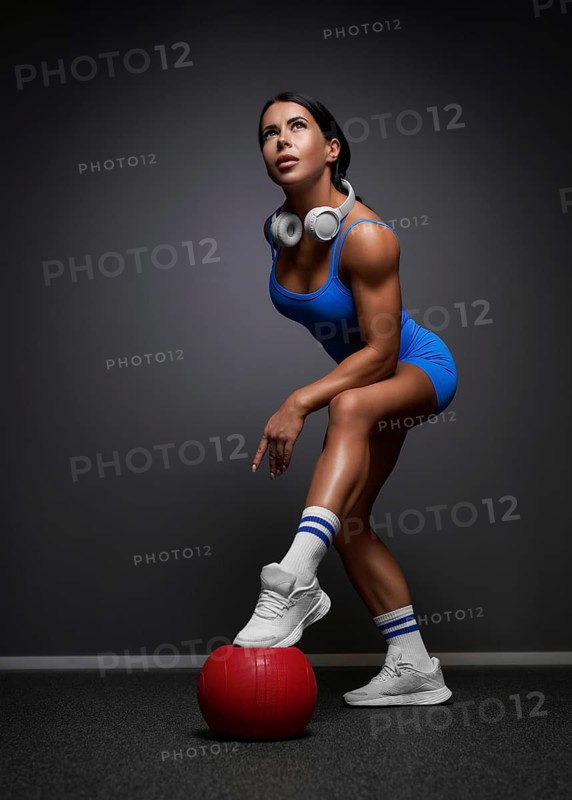 Sexy fitness woman. A beautiful athletic girl in a blue tracksuit posing in the studio. Red fitball
