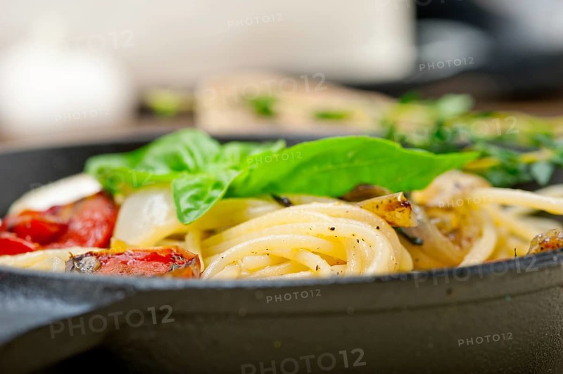 Italian spaghetti pasta with baked tomatoes basil and thyme sauce on a cast iron skillet