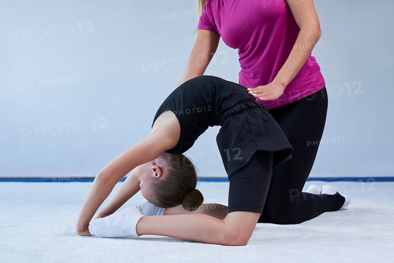 Training in the gym class. A little girl under the guidance of a trainer performs exercises. Gymnastics concept. Mixed media