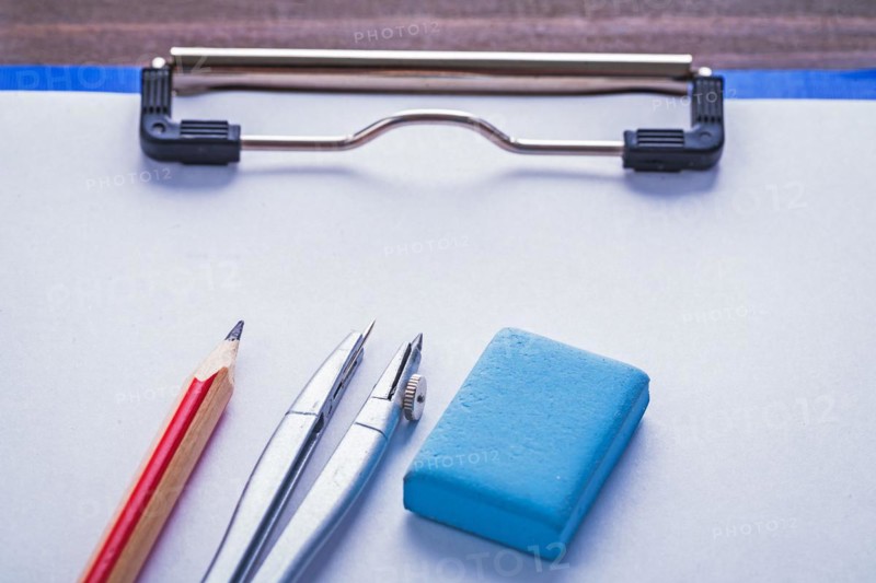 Eraser pencil compass on paper in clipboard on vintage wooden board learning concept