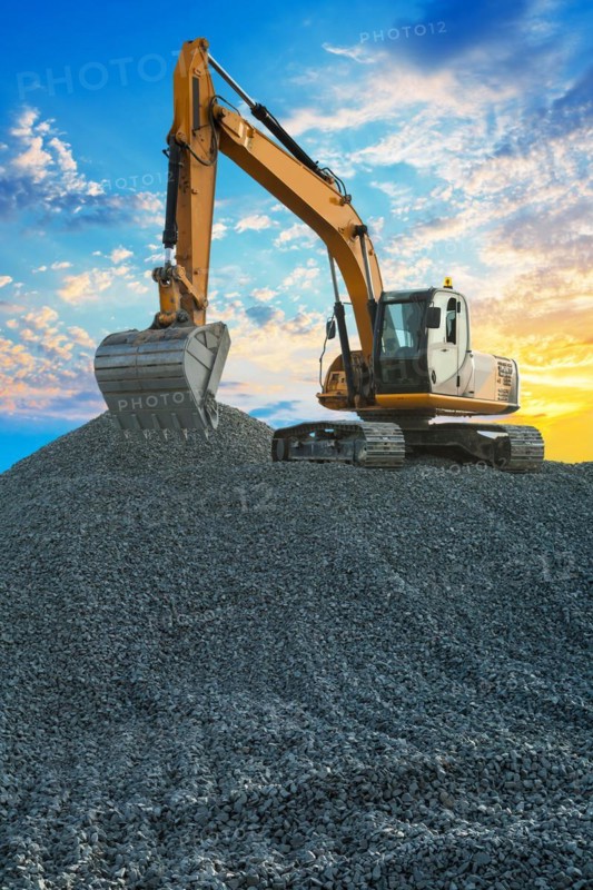 Excavator on large pile of gravel on a background of sunsetly sky