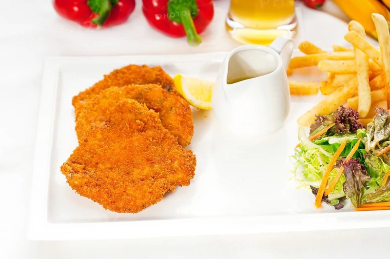 Classic breaded Milanese veal cutlets with french fries and vegetables on background