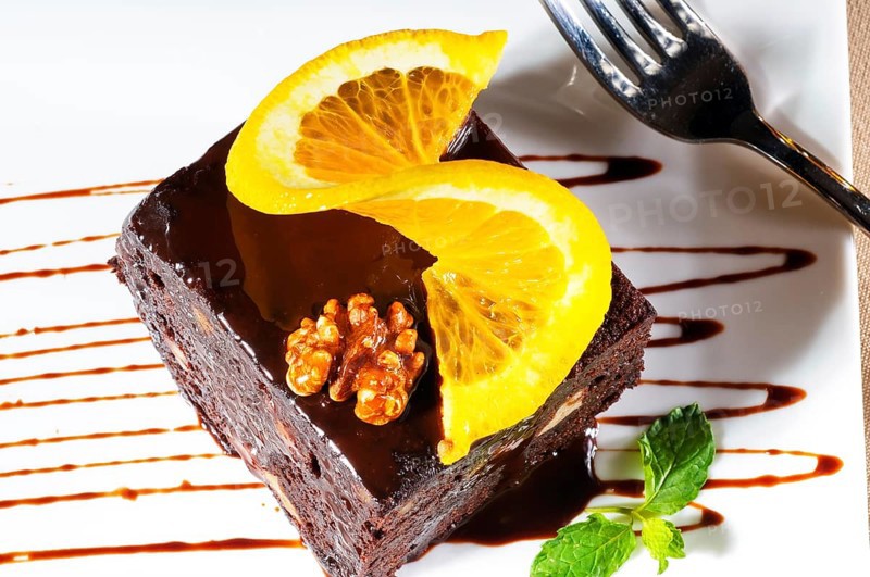Fresh baked delicious chocolate and walnuts cake with slice of orance on top and mint leaf
