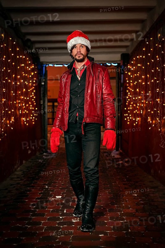 Man dressed as Santa Claus poses on a street decorated with garlands. New Year and Christmas concept. Mixed media