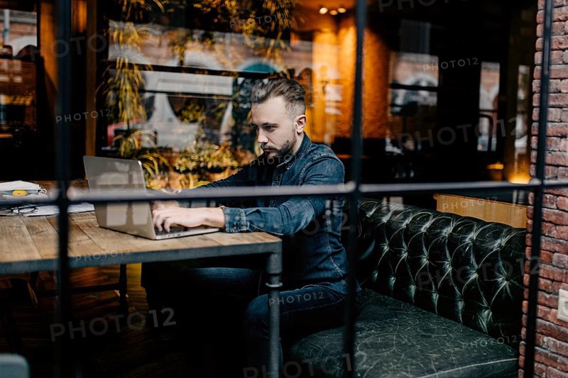 Young successful focused freelancer in a denim shirt working enthusiastically at a laptop in a covoking space
