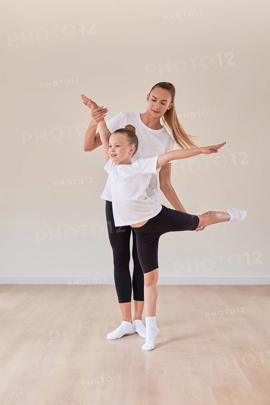 Beautiful woman teacher and a little girl perform dance movements in a bright studio. The concept of education