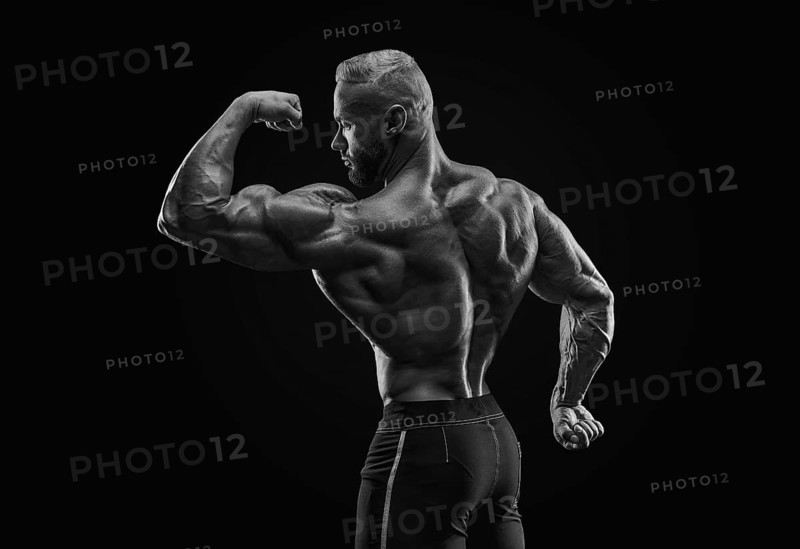 Silhouette of a strong bodybuilder. View from the back. Confident young fitness athlete with a powerful body and perfect abs. Black and white photography. Dramatic light