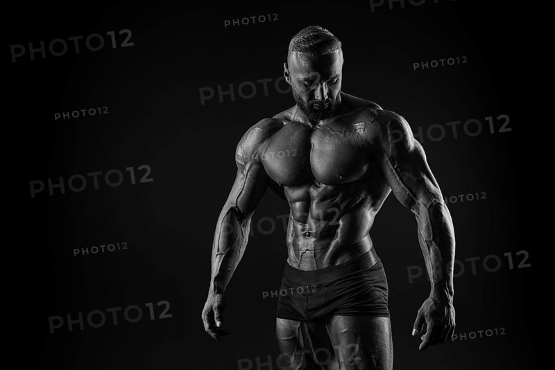 Silhouette of a strong bodybuilder. Confident young fitness athlete with a powerful body and perfect abs. Black and white photography. Dramatic light. Mixed media