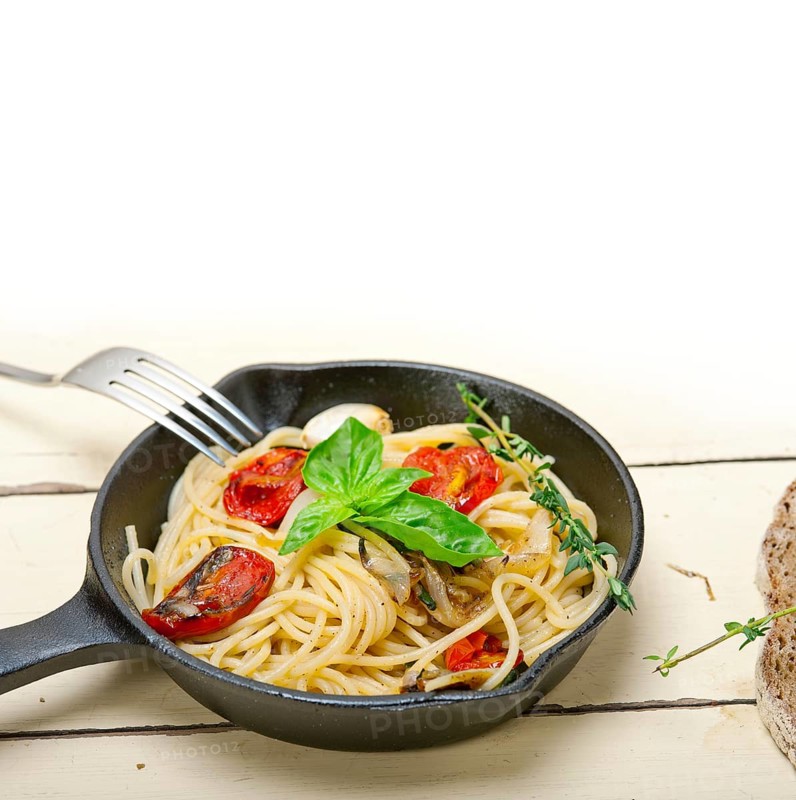 Italian spaghetti pasta with baked tomatoes basil and thyme sauce on a cast iron skillet