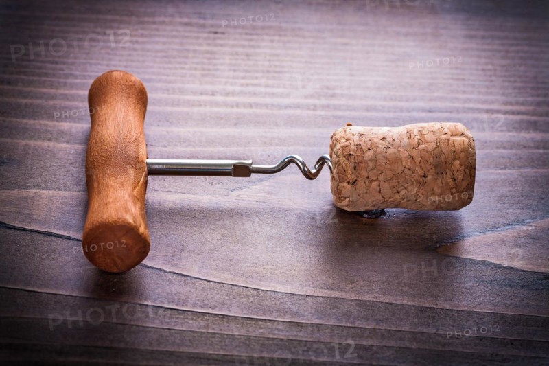Corkscrew twisted in corks of champagne on vinatge wooden board close up alcohol concept